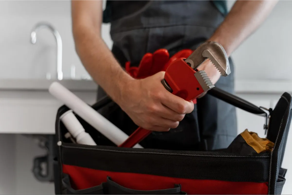 Close-up of hands placing a red pipe wrench into a black tool bag with red trim, showing professional plumbing equipment organization